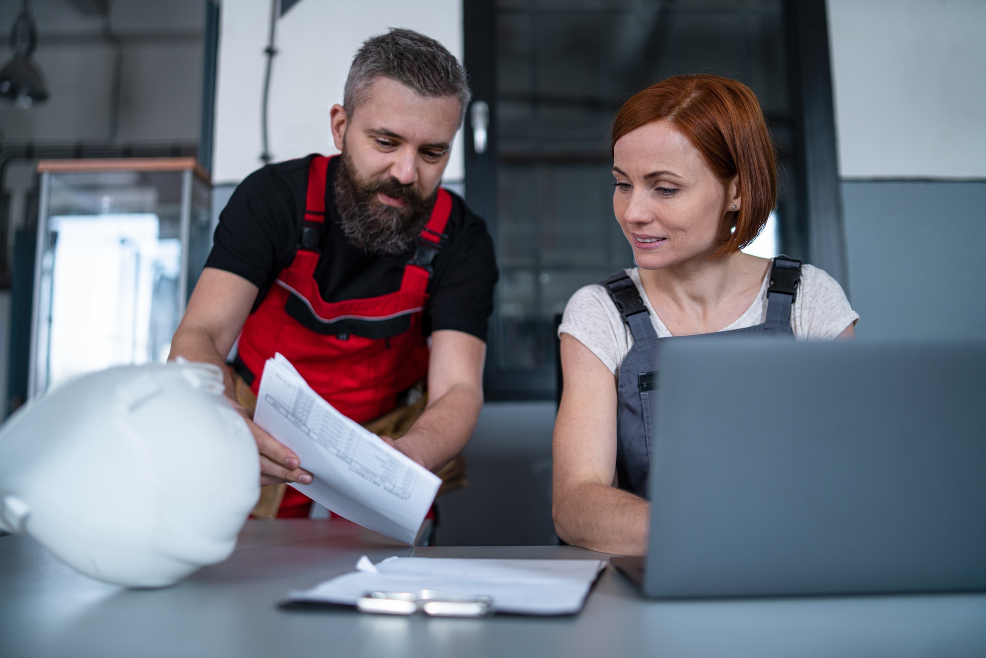 Group of workers or industry engineers with laptop indoors in factory, discussing issues